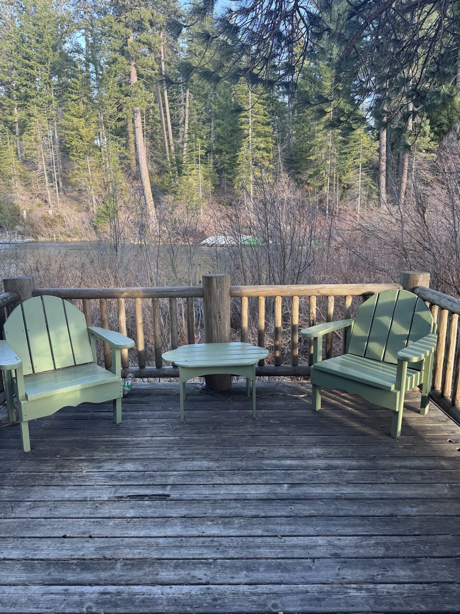 Green Adirondack chairs on a deck facing the water and pines